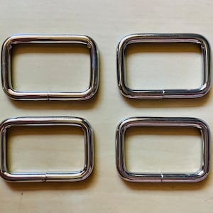 May include: Four silver metal D-rings, each with a smooth, rounded surface. The rings are arranged in two rows of two, with the top row slightly offset from the bottom row.
