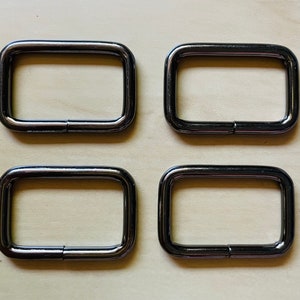 May include: Four silver metal D-rings, each with a rectangular shape and a smooth, polished finish.