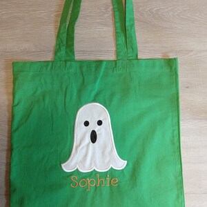 May include: Green canvas tote bag with a white ghost and the name "Sophie" embroidered in orange thread.