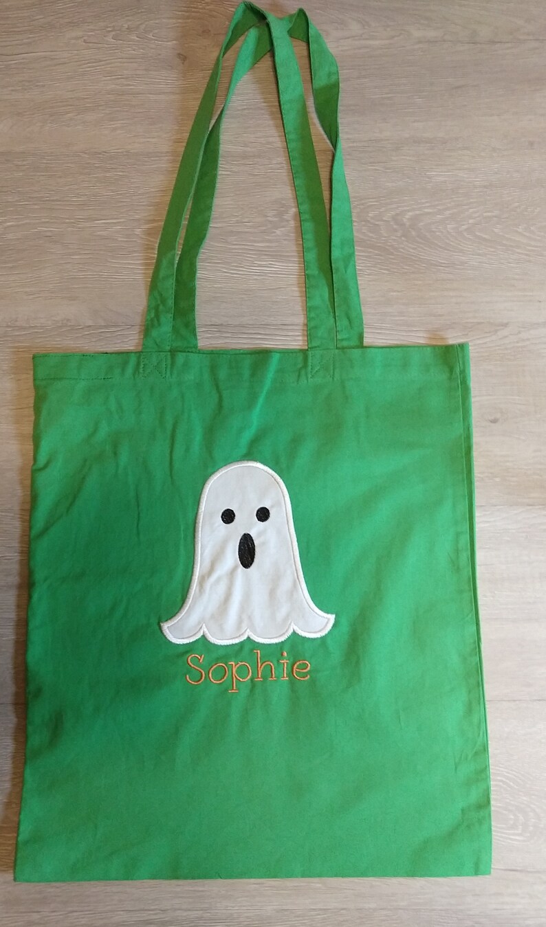 May include: Green canvas tote bag with a white ghost and the name "Sophie" embroidered in orange thread.