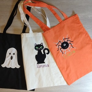 May include: Three Halloween-themed tote bags. One black bag with a white ghost, one white bag with a black cat, and one orange bag with a black spider.