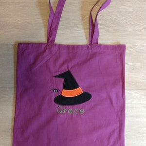 May include: Purple tote bag with a black witch hat and a spider embroidered on the front. The bag has the name "Grace" embroidered below the hat.