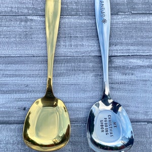 May include: Two spoons, one gold-colored and one silver-colored, are displayed. The gold spoon has a shiny finish. The silver spoon has the word "GRANDAD" engraved on the handle and "MY CHRISTMAS PUDDING SPOON" on the bowl.