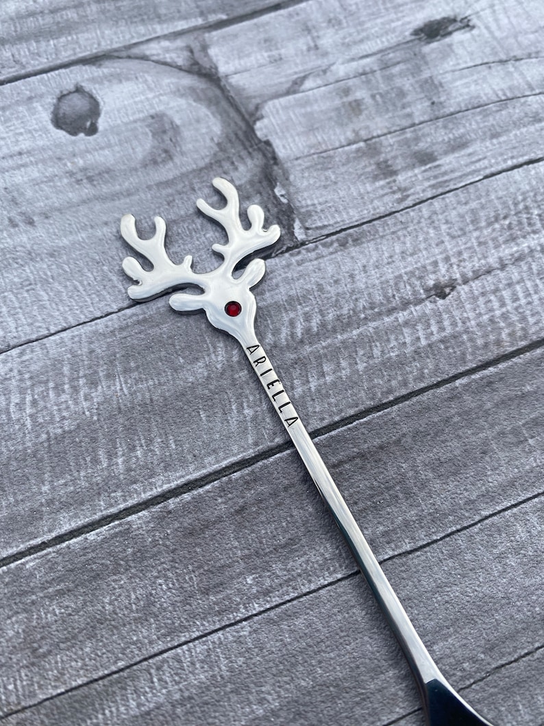 May include: Silver reindeer stirring spoon with a red rhinestone for the nose and the name "Ariella" engraved on the handle.