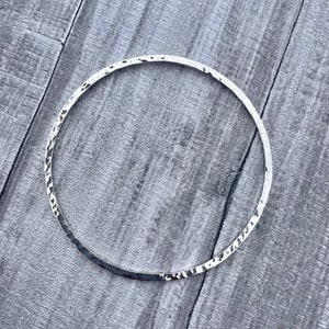 May include: A silver hammered bangle bracelet. The bracelet is smooth and shiny, with a hammered texture.