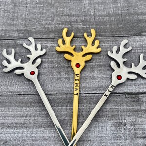 May include: Three gold and silver reindeer stir sticks with red rhinestones. The sticks are engraved with the names "Mommy", "Max", and "Mia".