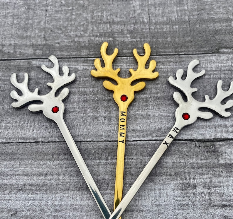 May include: Three gold and silver reindeer stir sticks with red rhinestones. The sticks are engraved with the names "Mommy", "Max", and "Mia".