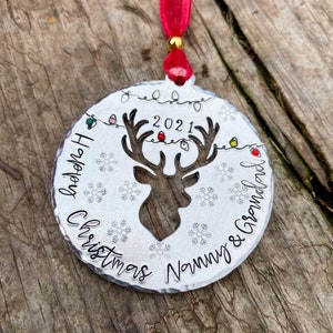 May include: A silver Christmas ornament with a reindeer silhouette, snowflakes, and the text "2021 Happy Christmas Nanny & Grandad".