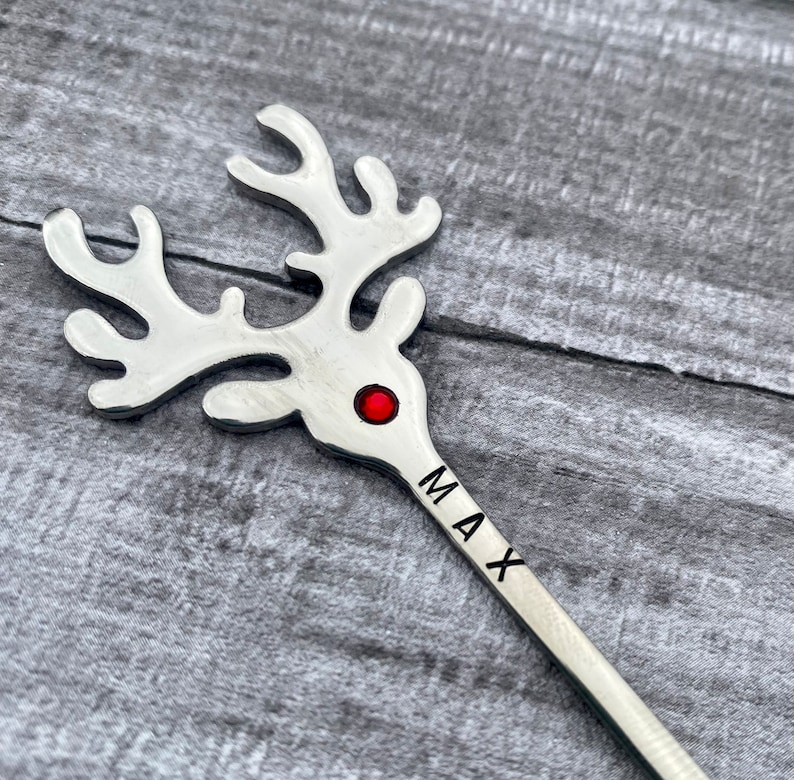 May include: Silver reindeer stir stick with a red jewel for the nose and the name "MAX" engraved on the handle.