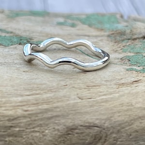 May include: A silver ring with a wavy design. The ring is on a wooden surface.