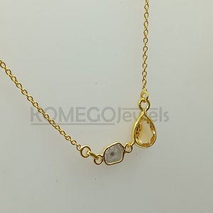 Puede incluir: Un collar de cadena dorada con una piedra preciosa de color marrón claro en forma de lágrima y una piedra preciosa transparente más pequeña de forma irregular.