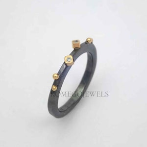 Könnte beinhalten: Ein schwarzer oxidierter Silberring mit goldenen Akzenten und kleinen Diamanten. Der Ring hat eine strukturierte Band mit kleinen goldenen Kugeln und quadratischen Fassungen für die Diamanten.
