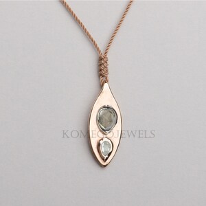 May include: A rose gold pendant necklace with a leaf-shaped design featuring two clear gemstones. The necklace is made with a brown cord.