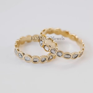 Puede incluir: Dos anillos de oro con una fila de pequeñas piedras transparentes y facetadas. Los anillos están apilados uno encima del otro.