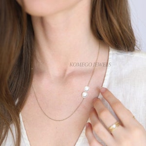 May include: A gold chain necklace with two white gemstone pendants. The necklace is worn by a model. The text "KOMEGO JEWELS" is visible in the image.