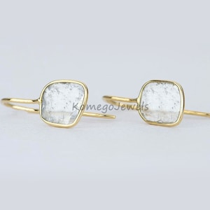 May include: A pair of gold earrings with clear, square-shaped stones. The stones have a textured, cloudy appearance.
