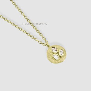 Può includere: Una collana d'oro con un ciondolo rotondo che presenta tre piccoli diamanti a forma di pera incastonati in un cerchio d'oro testurizzato. La collana è su uno sfondo bianco. KOMEO JEWELS è scritto nella parte superiore centrale dell'immagine.