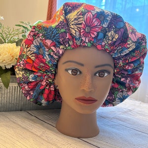 May include: A colorful floral print satin bonnet with a gathered top. The bonnet is worn on a mannequin head.