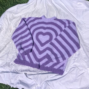 May include: A purple and light purple striped crocheted sweater with a heart design in the center.