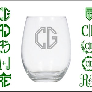 May include: A clear glass wine glass with a monogrammed design. The monogram is in a gray color and is in the center of the glass. The glass is sitting on a white background. There are several other monogram designs in green on the left and right sides of the image.