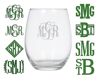May include: A clear stemless wine glass with a monogram in the center. Several green monogram designs are displayed around the glass, showcasing different fonts and styles. The monograms are in various shapes, including a diamond and a laurel wreath.