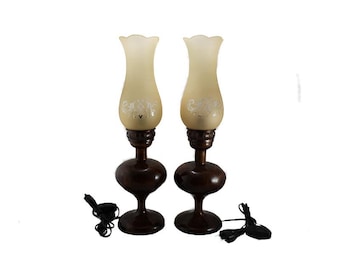 May include: A pair of brown wooden table lamps with cream colored glass shades. The shades have a floral design.
