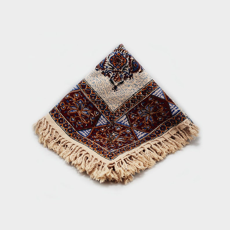 May include: A square, cream-colored tablecloth with a brown, blue, and white floral pattern. The tablecloth has a fringe border.