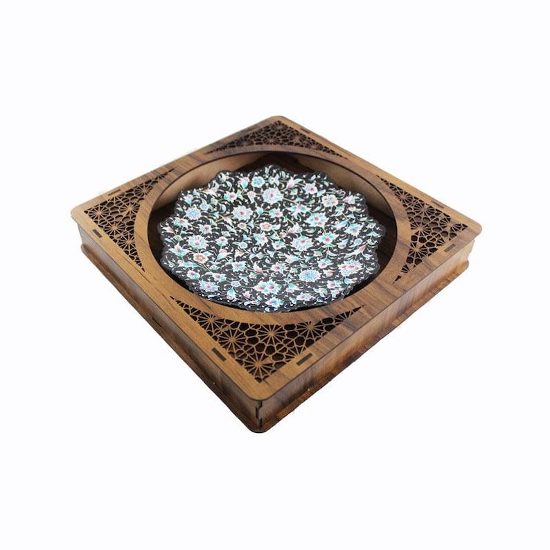 May include: A square wooden box with a decorative floral patterned coaster. The coaster has a black background with a colorful floral design. The box has a carved geometric design around the edges.