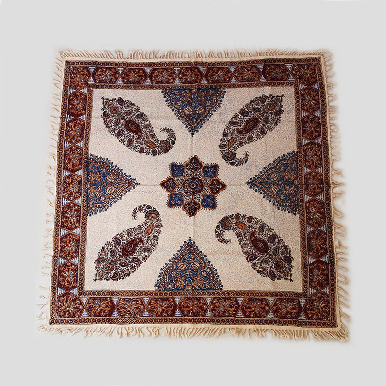May include: A white tablecloth with a brown and blue paisley pattern. The tablecloth has a fringe border.