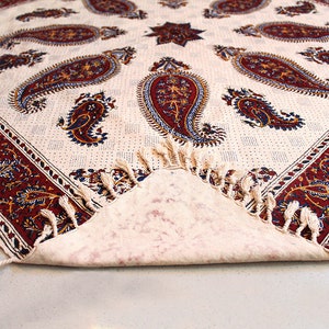 May include: A white tablecloth with a paisley pattern in shades of red, blue, and gold. The tablecloth has a fringe border and is folded in half.