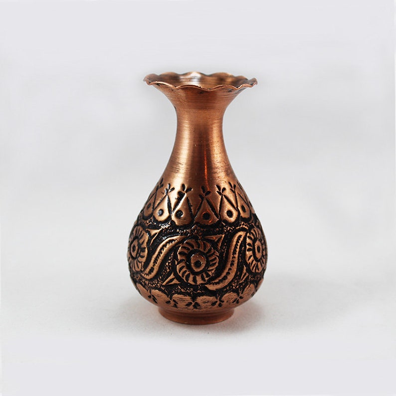 May include: A small copper vase with an intricate embossed design. The vase has a scalloped rim and a rounded body.