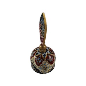 Peut inclure: Une cloche décorative dotée d'un manche pointu et d'un corps arrondi, tous deux ornés de motifs peints à la main dans des tons rouge foncé, crème, noir et doré. La surface présente des motifs floraux et géométriques détaillés sur l'ensemble.