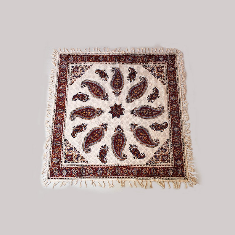 May include: A white tablecloth with a red and blue paisley pattern. The tablecloth has a fringe border.