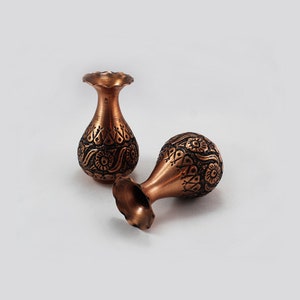 May include: Two small copper vases with intricate floral designs. The vases are a reddish-brown color and have a slightly rounded shape.