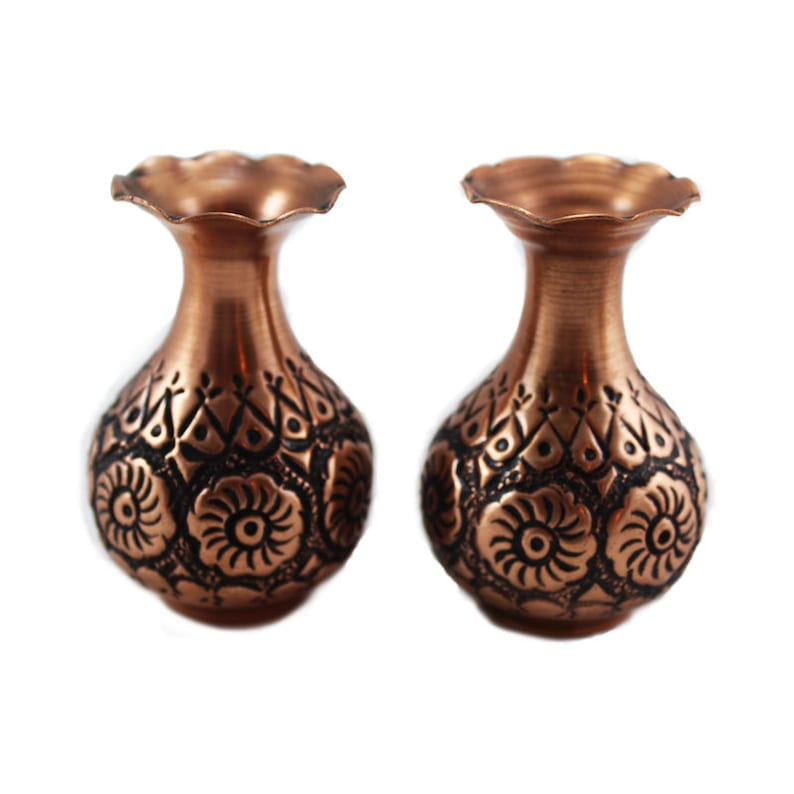 May include: Two small copper vases with intricate floral designs. The vases are a reddish-brown color and have a scalloped rim.
