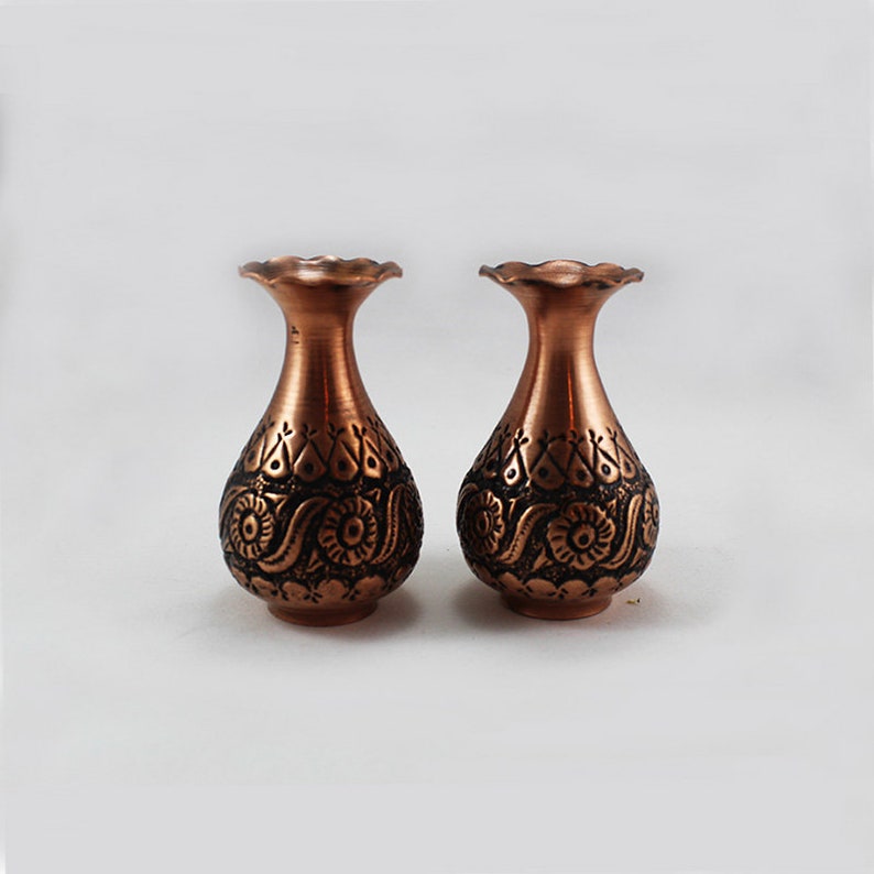May include: Two small copper vases with intricate floral designs. The vases are a deep copper color and have a slightly flared opening.