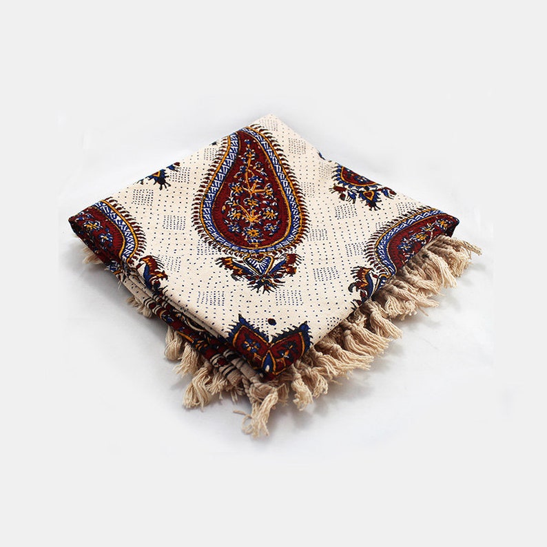 May include: A white cotton throw blanket with a paisley pattern in shades of red, blue, and yellow. The blanket has a fringe border.