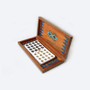Op de afbeelding: Een open houten speldoos met ingewikkelde blauwe en gouden inlegwerk. De doos bevat een wit plastic dienblad met 36 kleine ronde gaten.