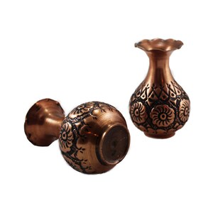 May include: Two small copper vases with intricate floral designs. The vases are about 4 inches tall and have a round body with a narrow neck.