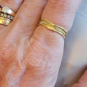 May include: A gold band ring with a twisted design. The ring is worn on a person's finger.