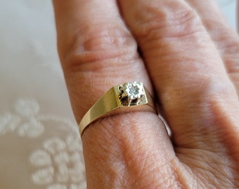 Puede incluir: Un anillo de banda de oro con un solo diamante claro engastado en el centro.