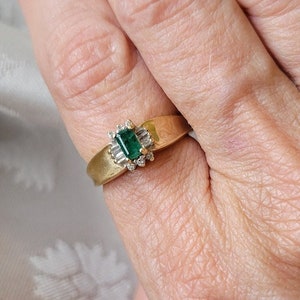Könnte beinhalten: Ein goldener Ring mit einem grünen Smaragd, der von kleineren Diamanten umgeben ist.