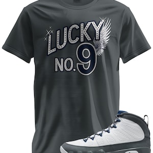 May include: A dark gray t-shirt with the text "LUCKY NO. 9" in white and navy blue, with a wing graphic. A white, gray, and navy blue sneaker is in the foreground.