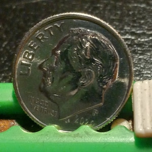 May include: A silver US dime coin with the words "Liberty" and "In God We Trust" on the front. The coin features a profile of a man with short hair.