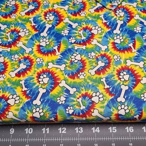 May include: A colorful tie-dye fabric with a repeating pattern of white paw prints and bone shapes. The fabric is yellow, blue, red, and green.