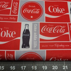 Op de afbeelding: Rode en witte stof met een herhalend patroon van Coca-Cola-logo's, flessen en de tekst "Enjoy Coke" en "Coke adds life".