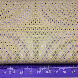 Könnte beinhalten: Gelber Stoff mit einem sich wiederholenden Muster aus kleinen weißen, blauen und roten geometrischen Formen. Der Stoff wird mit einem Lineal in Zoll gemessen.