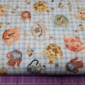 Puede incluir: Tela a cuadros azules y blancos con un patrón repetido de teteras y osos de peluche. Las teteras están decoradas con flores, corazones y las palabras "Much Loved Tea Company".