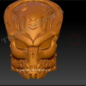 May include: A golden-colored, detailed 3D model of a Predator mask, showcasing intricate mechanical and organic design elements. The mask features a prominent brow, eye sockets, and a mouth area with detailed teeth. The text "2023 TECNOPRINTO" is visible.