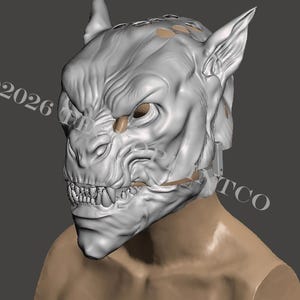 Op de afbeelding: Een gedetailleerd, grijs monster masker met scherpe tanden, puntige oren en een getextureerde huid. Het masker is gebeeldhouwd met ingewikkelde details, wat wijst op een wezenachtig uiterlijk. Het copyrightsymbool en het jaar 2026 zijn zichtbaar.